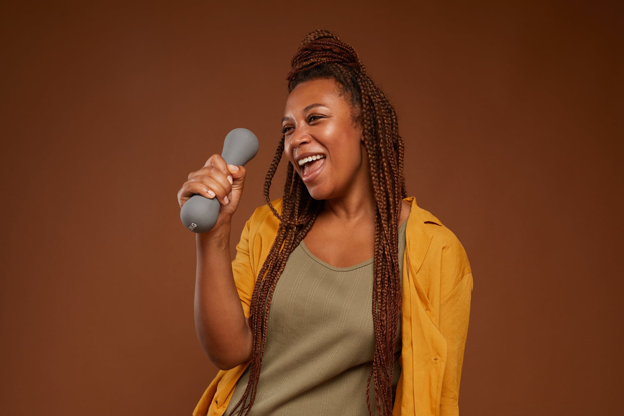 African American woman with a dumbell in her hands using it as a mock microphone