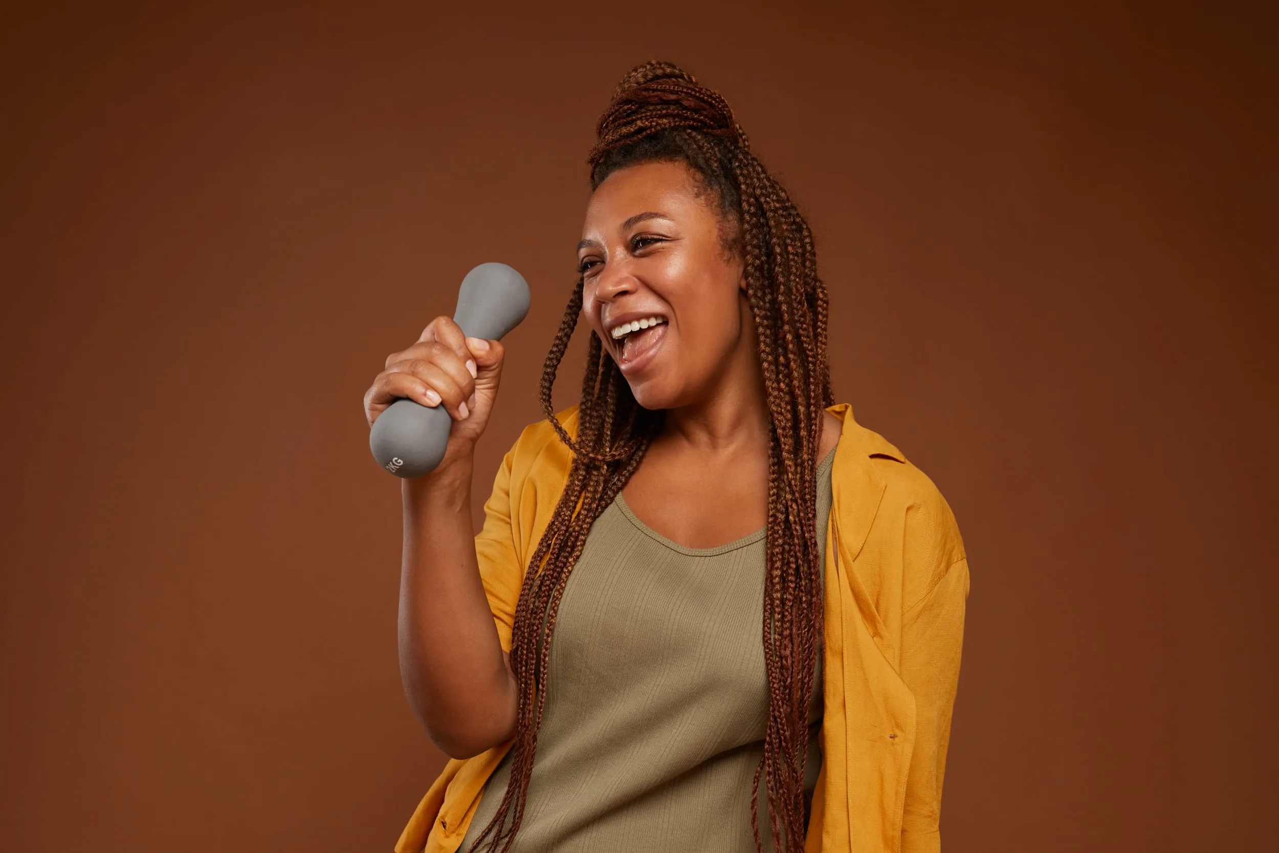 African American woman with a dumbell in her hands using it as a mock microphone